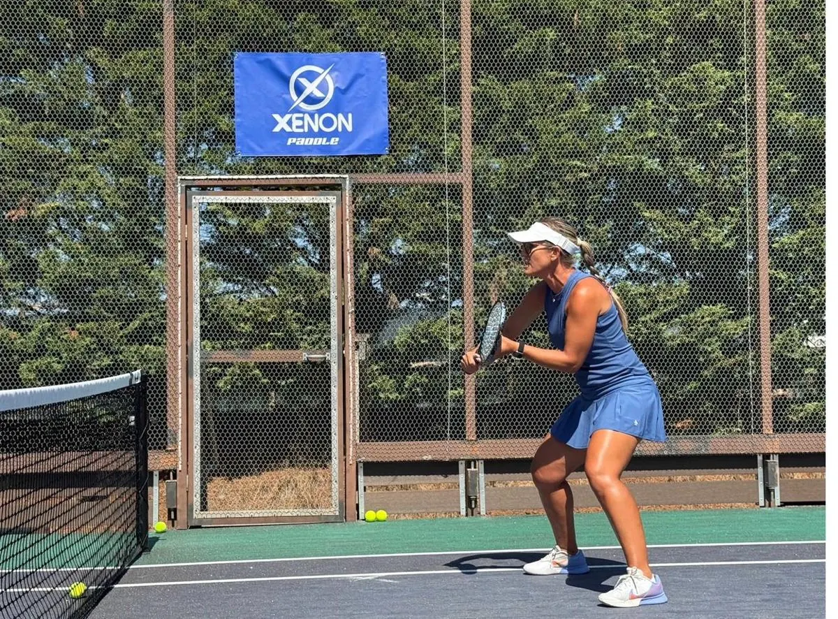 Coach in ready position on court with Xenon banner